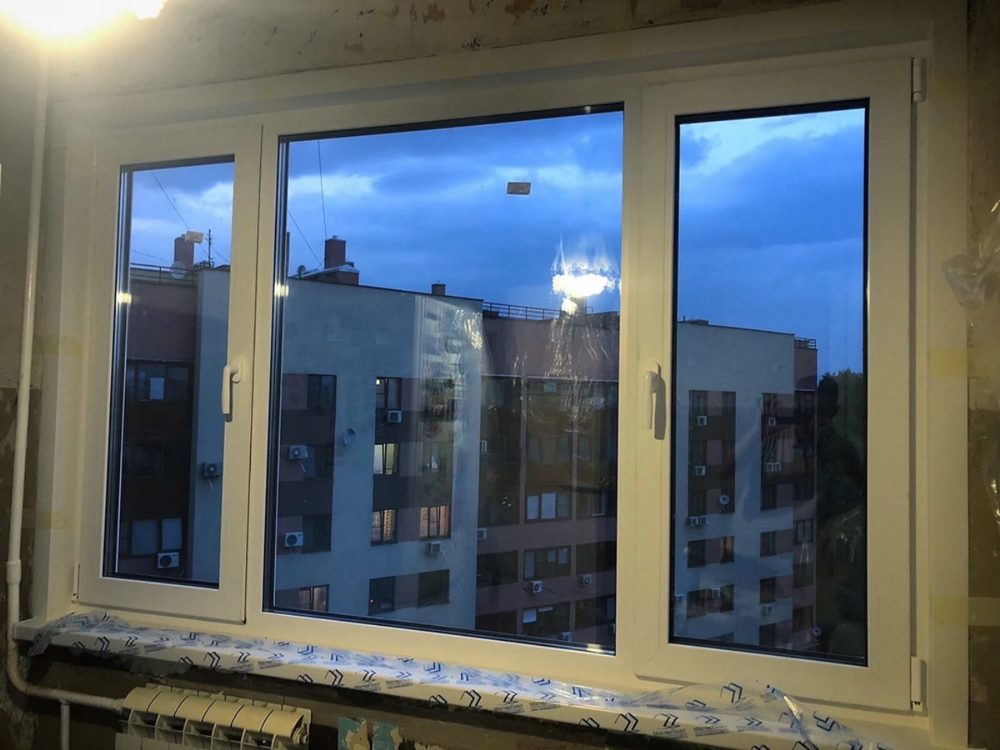 Широкое окно в квартире на стадии ремонта, вечерний вид на город